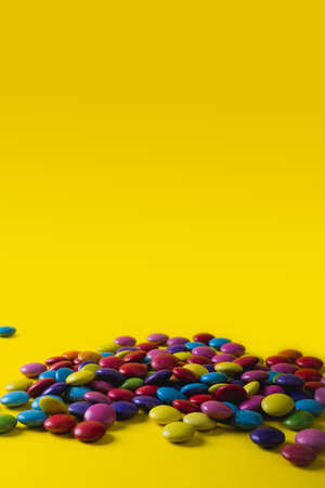 Pile of colorful chocolate candies with copy space against yellow background. unaltered, unhealthy...