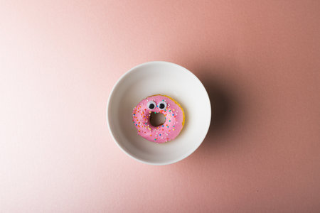 Directly above view of pink donut with googly eyes in plate around copy space on colored background. unaltered, unhealthy eating and sweet food concept.の写真素材