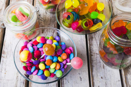 High angle view of multi colored various lollipops and candies in bowls and jars on wooden table. unaltered, unhealthy eating and sweet food concept.の写真素材