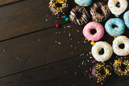 Directly above view of fresh various donuts with sprinklers and candies on wooden table. unaltered, unhealthy eating and sweet food concept.の写真素材