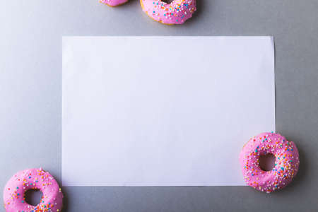 Directly above view of blank white paper with copy space amidst pink donuts on gray background. unaltered, unhealthy eating and sweet food concept.の写真素材
