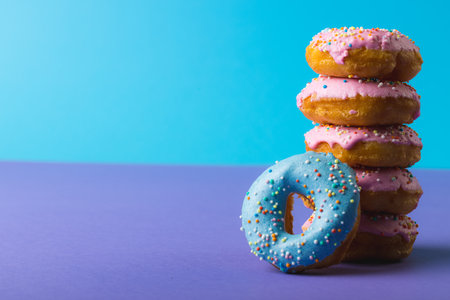 Close-up of fresh donuts with sprinklers stacked against two tone colored background with copy space. unaltered, unhealthy eating and sweet food concept.の写真素材