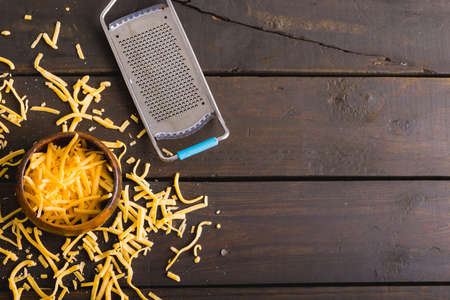 Directly above shot of grated yellow cheese and bowl by grater on wooden table, copy space. unaltered, food and dairy product.の写真素材
