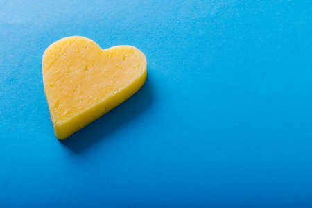 High angle view of heart shaped yellow cheese on blue background, copy space. unaltered, food, studio shot and dairy product.の写真素材