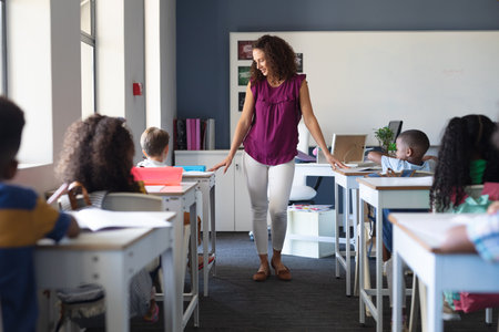 Caucasian female teacher with multiracial elementary school children at desk in classroom. unaltered, education, teaching, childhood, occupation and school concept.の写真素材