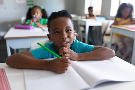 African american elementary schoolboy making face while sitting at desk during class. unaltered, education, confusion, childhood, learning and school concept.の写真素材