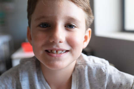 Close-up portrait of smiling elementary schoolboy sitting at desk in classroom. unaltered, education, childhood, learning and school concept.の写真素材