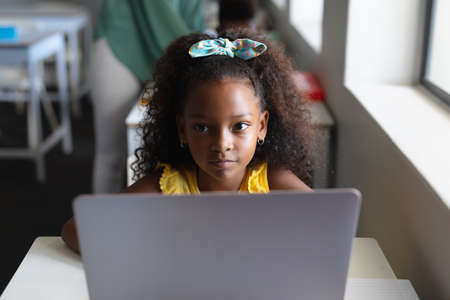 African american elementary schoolgirl looking away while sitting with laptop during computer class. unaltered, education, childhood, learning, wireless technology and school concept.の写真素材