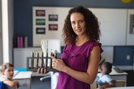 Portrait of caucasian young female teacher showing seedlings test tubes while teaching in classroom. unaltered, education, teaching, science, occupation and school concept.の写真素材