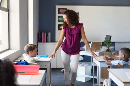 Caucasian female teacher teaching multiracial elementary school children at desk in classroom. unaltered, education, teaching, childhood, occupation and school concept.の写真素材