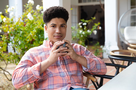 Happy biracial man sitting on garden terrace drinking coffee outside house. Inclusivity, domestic life, leisure time and happiness concept.の写真素材