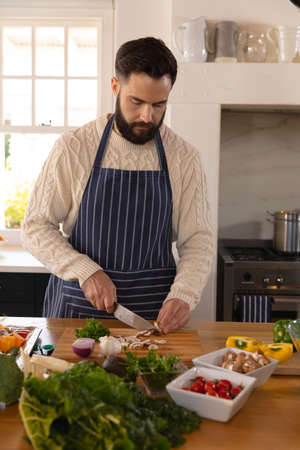 Caucasian man preparing food, concentrating on chopping vegetables, wearing apron in kitchen....
