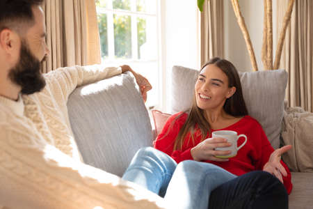 Happy caucasian couple sitting on couch in living room, talking and drinking coffee. Domestic life,...