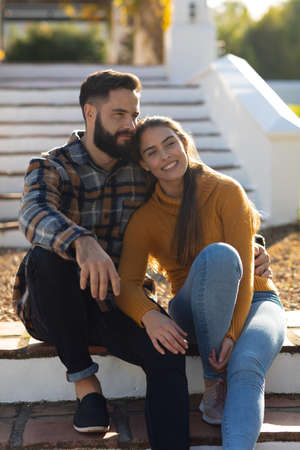 Happy caucasian couple sitting on terrace steps smiling and embracing in sunny autumn garden. Domestic life, leisure time, romance and togetherness concept.の写真素材