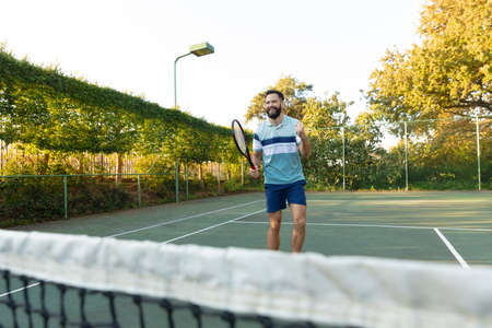 Happy caucasian man playing tennis celebrating on outdoor tennis court. Sport, healthy hobbies, competition, fitness and leisure time concept.の写真素材