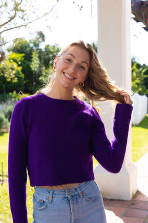 Portrait of smiling caucasian woman standing on garden terrace, holding hair and looking to camera. Domestic life, heath and happiness, spending time alone at home.の写真素材