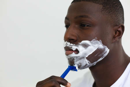 African american man shaving face in bathroom. Inclusivity, self care, health and hygiene, spending time alone at home.の写真素材