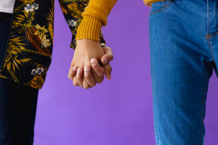 Mid section of biracial male couple holding hands on purple background. Lgbt and pride concept.の写真素材