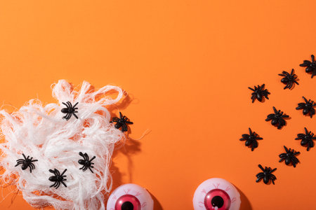 Multiple spider toys forming a spider web and scary eyes toys with copy space on orange background. halloween festivity and celebration conceptの写真素材