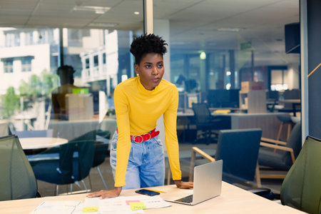 Thoughtful african american woman with laptop standing in cabin at modern office. business and office conceptの写真素材