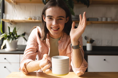 Portrait of non-binary trans woman with coffee cup smiling in the kitchen at home. concept of gender fluidityの写真素材