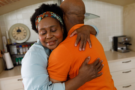 Senior african american couple spending time at home together, standing in kitchen, embracing and...