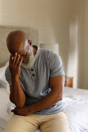 Senior african american man spending time at home, sitting on bed, holding his head. isolating...