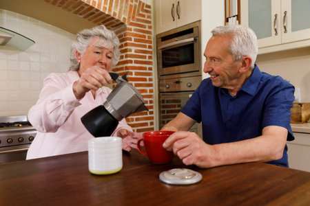 Senior caucasian couple spending time at home together, sitting in kitchen, pouring coffee into cup. isolating during virus quarantine lockdown.の写真素材