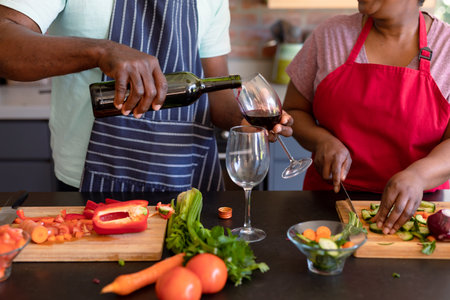 Midsection of african american senior couple cooking together in kitchen, drinking wine. retirement...