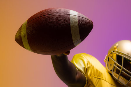African american male american football player holding ball with neon yellow and purple lighting. Sport, movement, training and active lifestyle concept.の写真素材