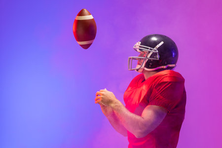 Caucasian male american football player holding ball with neon blue and purple lighting. Sport, movement, training and active lifestyle concept.の写真素材