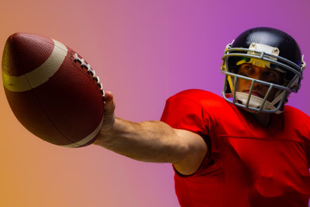 Caucasian male american football player holding ball with neon yellow and purple lighting. Sport, movement, training and active lifestyle concept.の写真素材