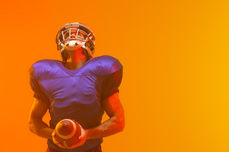 Caucasian male american football player holding ball with neon orange lighting. Sport, movement, training and active lifestyle concept.の写真素材