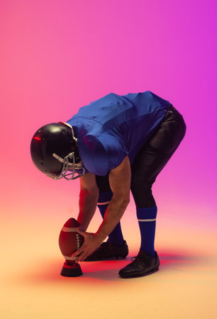 Caucasian male american football player holding ball with neon pink lighting. Sport, movement, training and active lifestyle concept.の写真素材