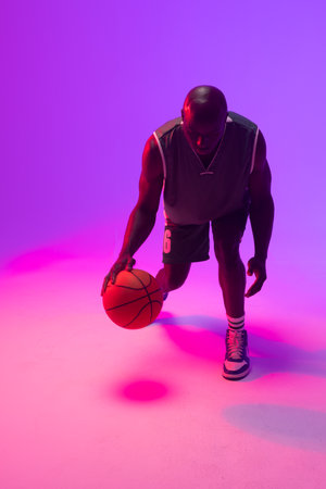 Image of african american basketball player bouncing basketball on neon purple background. Sports...