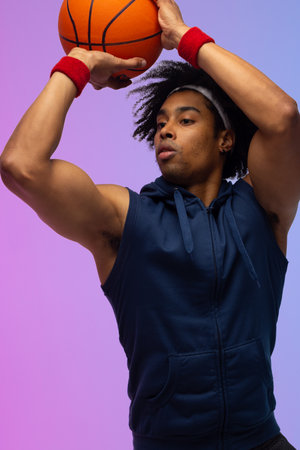 Image of biracial basketball player throwing basketball on purple to blue background. Sports and...