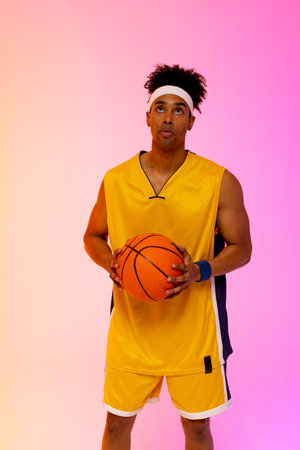 Image of biracial basketball player with basketball on pink to orange background. Sports and competition concept.の写真素材