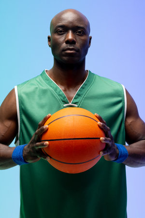 Image of portrait of african american basketball player with basketball on green to blue background....
