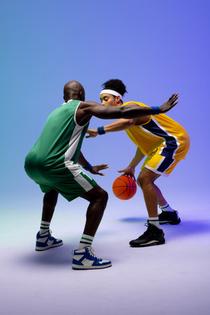 Image of two diverse basketball players with basketball playing on purple to blue background. Sports and competition concept.の写真素材