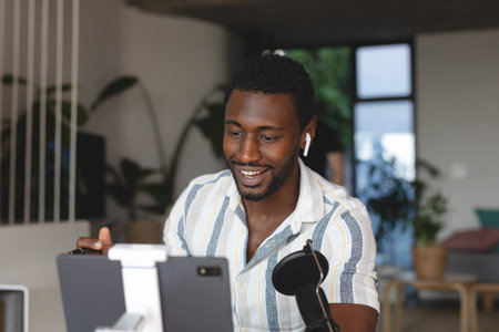 Happy african american man sitting at table in kitchen using tablet for video call. Spending quality time at home alone.の写真素材