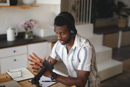Happy african american man sitting at table in kitchen using laptop for video call. Spending quality...