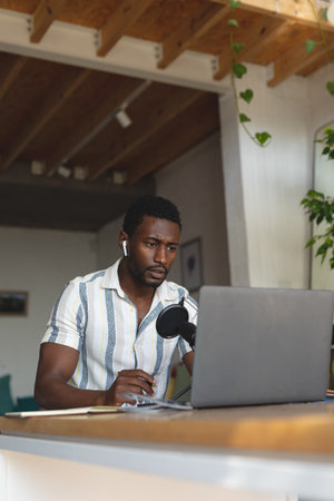 Happy african american man sitting at table in kitchen using laptop for video call. Spending quality time at home alone.の写真素材