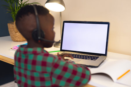 Smiling african american boy learning, using headphones and laptop with copy space at home. Home education, distance learning.の写真素材