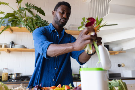 Happy african american man standing in kitchen and cleaning waste. Spending quality time at home alone.の写真素材