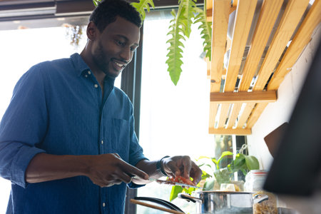 Happy african american man standing in kitchen and cooking dinner. Spending quality time at home alone.の写真素材