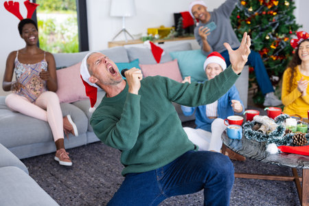 Image of happy caucasian man singing karaoke celebrating christmas at home with diverse friends. Christmas, celebration, tradition, friendship, inclusivity and lifestyle concept.の写真素材