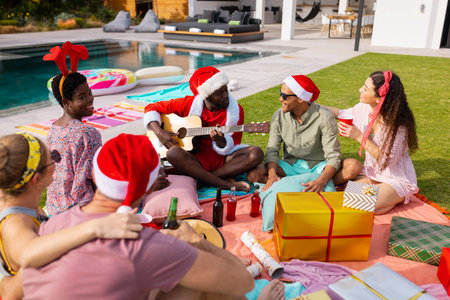 Happy diverse friends with santa hats having picnic in garden at christmas. Christmas, celebration,...