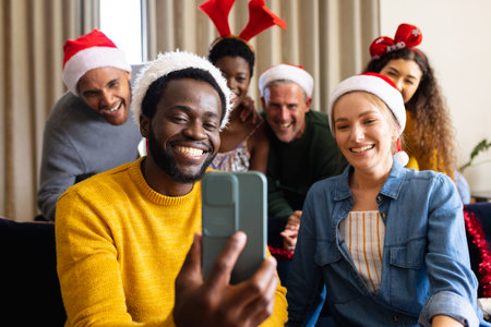 Image of happy diverse friends celebrating christmas at home making smartphone video call. Christmas, celebration, tradition, friendship, inclusivity and lifestyle concept.の写真素材