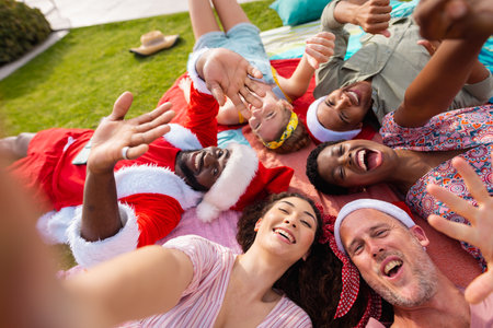 Portrait of happy diverse friends with santa hats in garden at christmas. Christmas, celebration, friendship, inclusivity and lifestyle concept.の写真素材