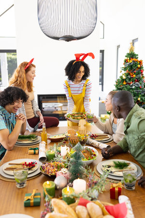 Happy diverse friends sitting at table and having dinner at christmas. Christmas, celebration, friendship, inclusivity and lifestyle concept.の写真素材